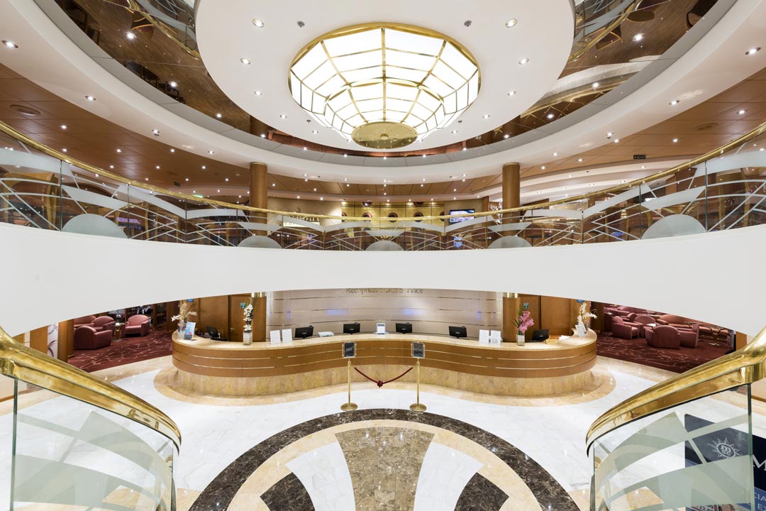 Opulent hotel lobby with a reception desk and plush seating areas under a circular skylight.